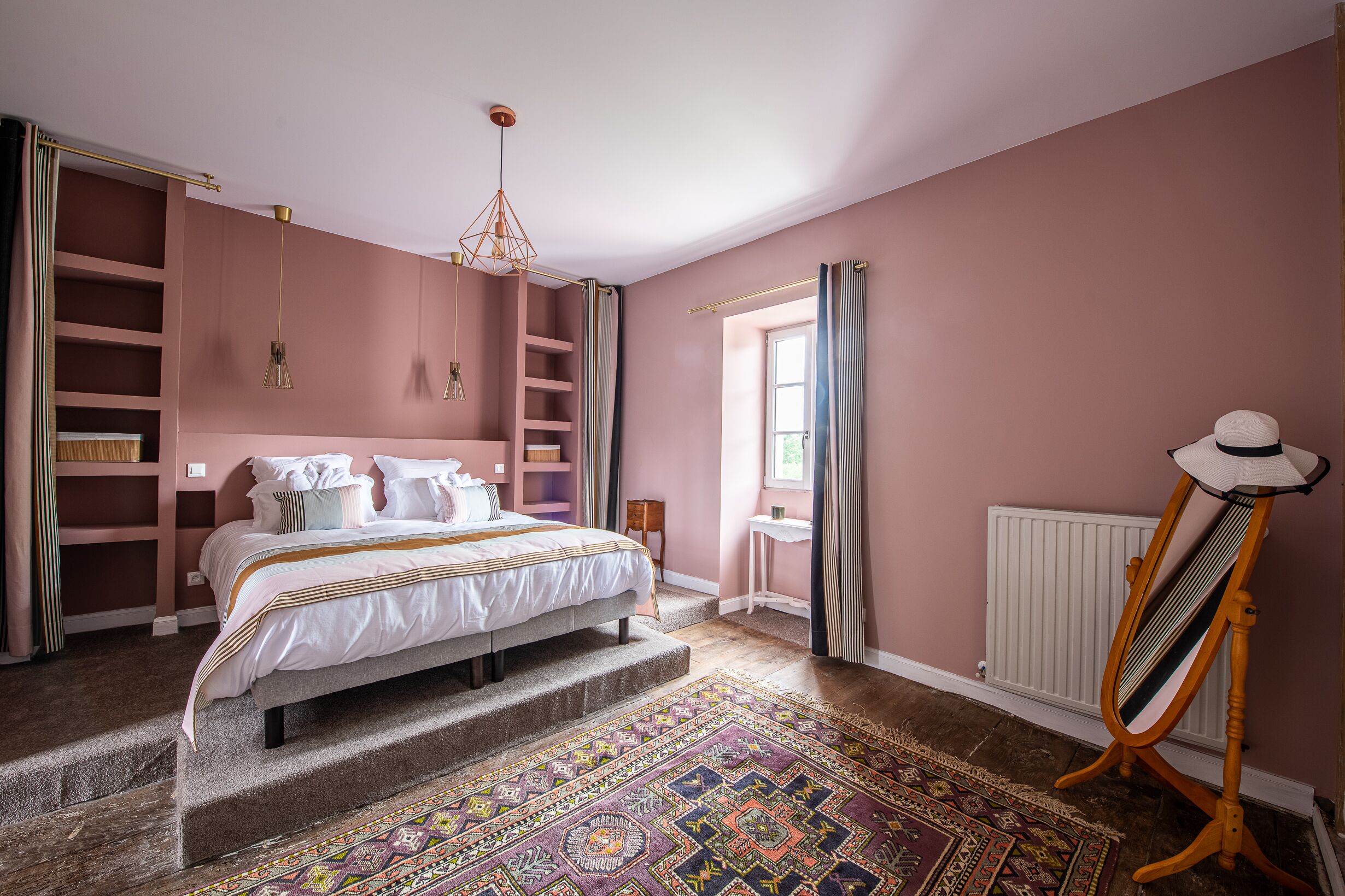 Ein Schlafzimmer mit Bett, einem Heizkörper, einem Fenster mit Vorhängen und einem gemusterten Teppich.