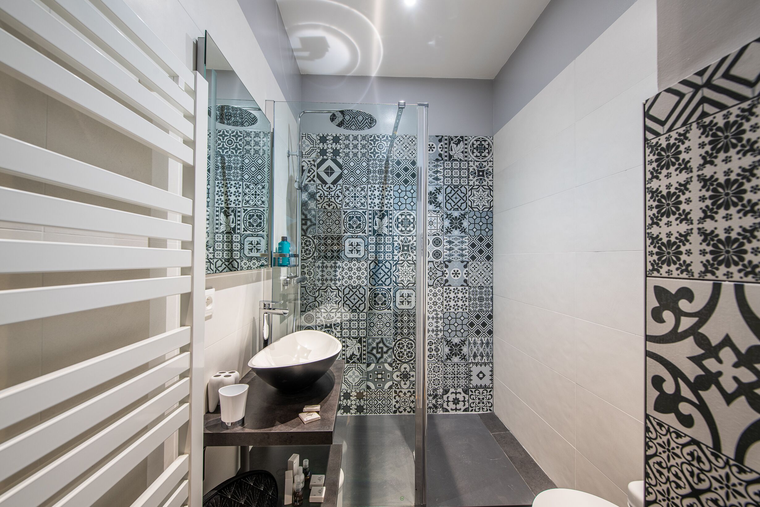 A modern bathroom with a large glass shower, a white sink, and patterned tiles.