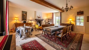 A dining area with a wooden table, chairs, and a chandelier. There is a fireplace and a bookshelf in the background. - The noble house of Luroa built in 1505. (Cambo-les-Bains)