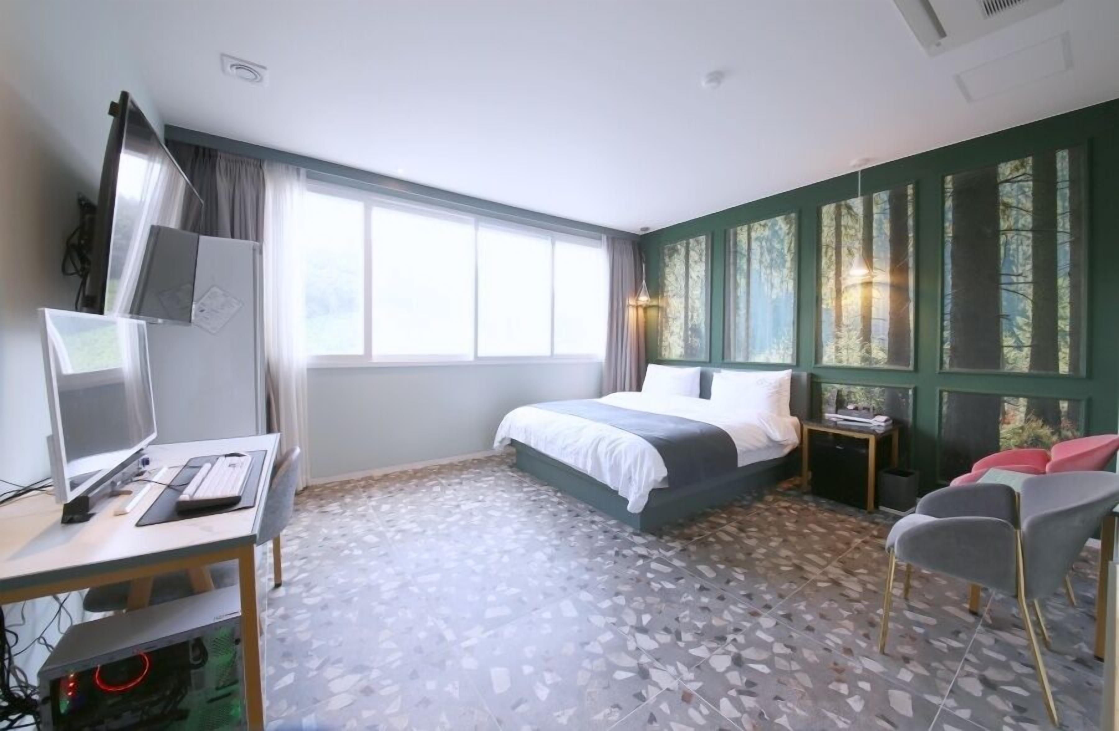 Una habitación de hotel con cama, escritorio con computadora, silla y ventana con cortinas.