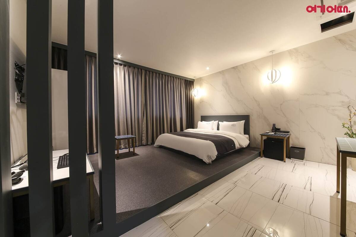 A modern hotel room with a bed, bedside table, and a desk with a chair.