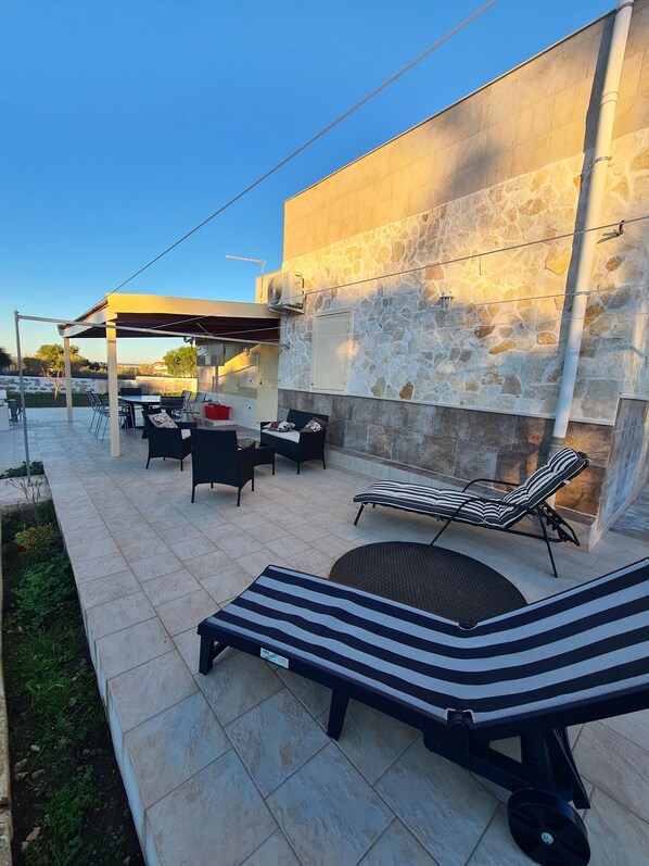 An outdoor patio with lounge chairs, a table, and a covered seating area. - Beautiful villa near Torre Ovo, 800 meters from the sea. (Monacizzo-librari-truglione)