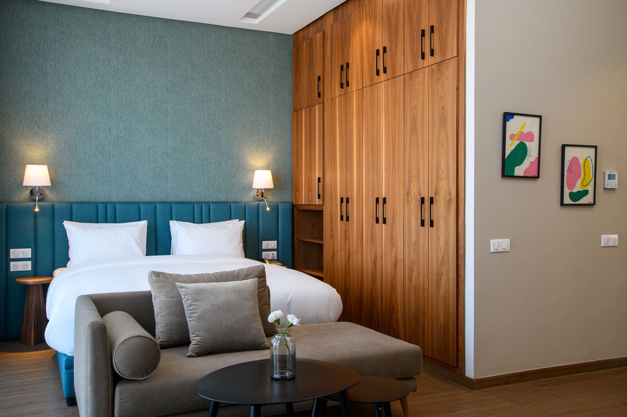 A hotel room with a bed, two bedside lamps, a sofa, a small table, and a wooden wardrobe.