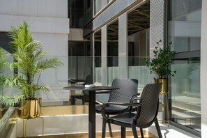 Un área de estar al aire libre con diseño moderno, con dos sillas y una mesa, rodeada de paredes de vidrio y plantas en macetas.