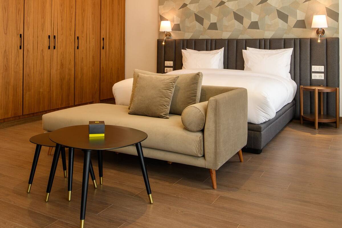 Quarto de hotel moderno com uma cama grande, um sofá, uma mesa pequena e armários de madeira.