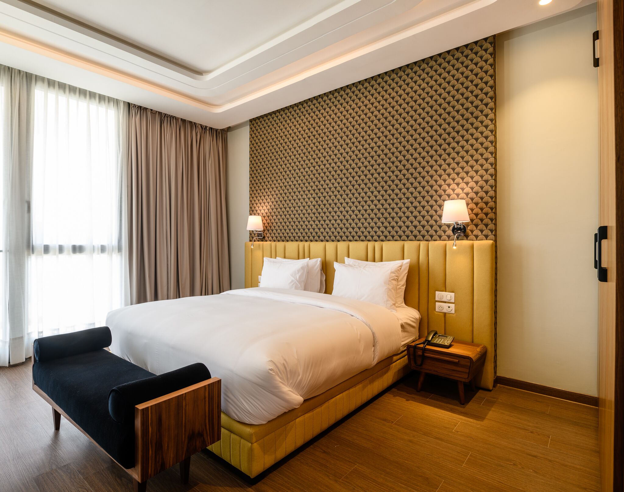 A hotel room with a large bed, bedside lamps, a small table, and a chair.