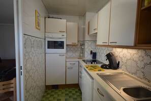 Uma cozinha compacta com armários brancos, forno embutido, micro-ondas, máquina de café e pia.