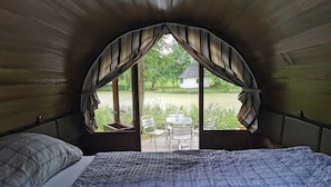 A cozy room with a bed, a window with curtains, and a view of a garden and outdoor seating area.