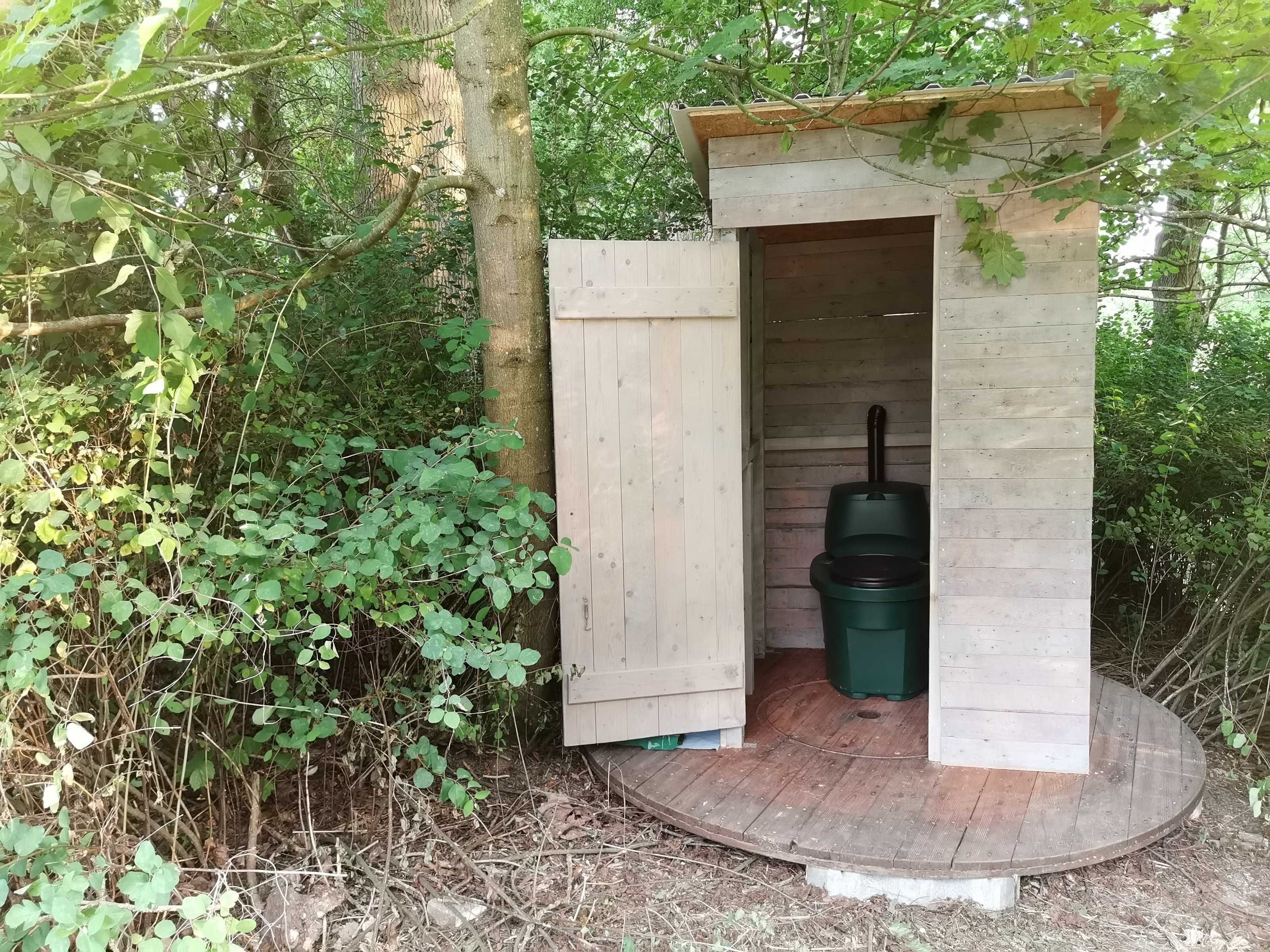 A small wooden structure with a door, a green trash bin, and a wooden platform.