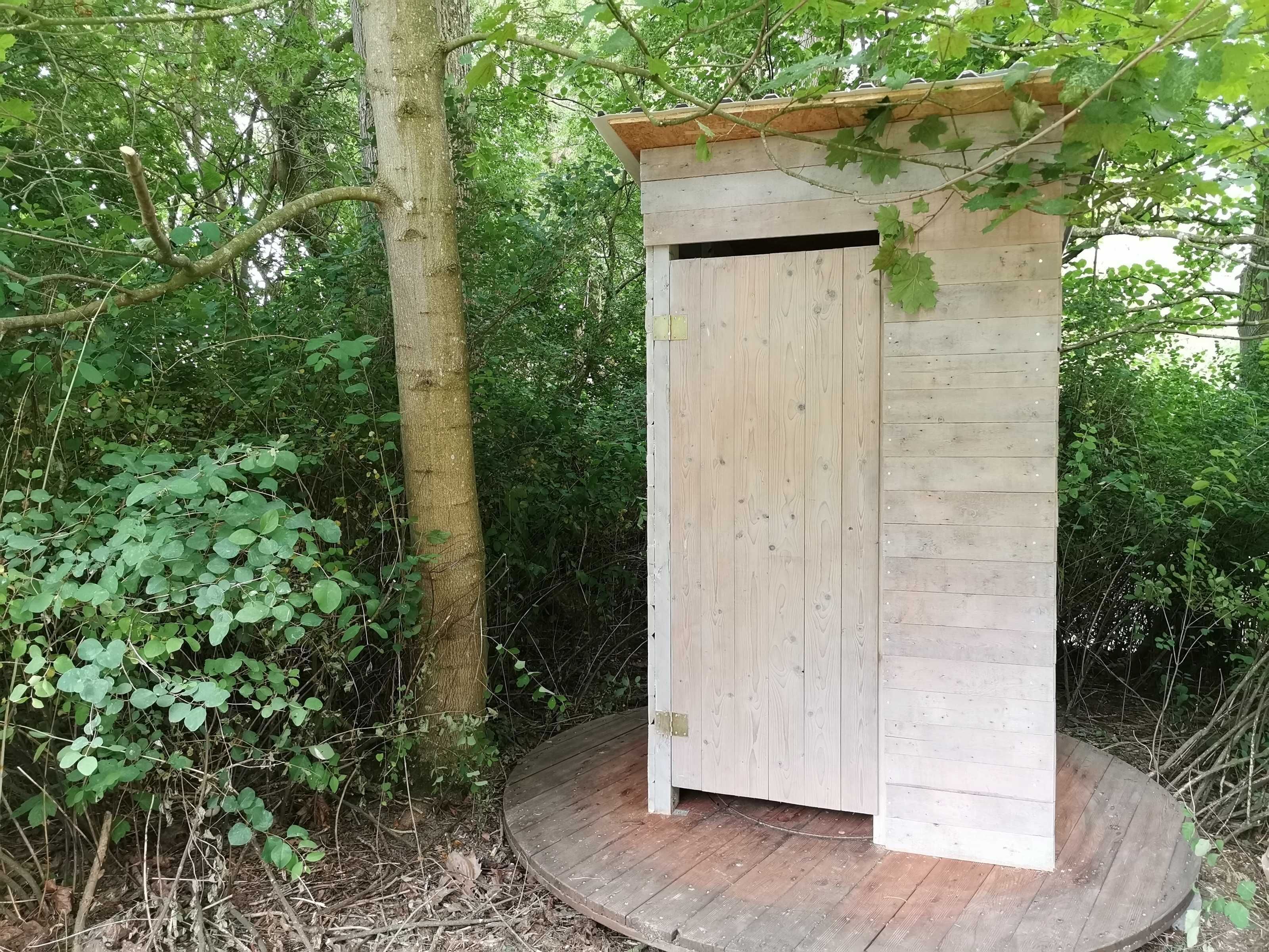 Une structure en bois dotée d’une porte, entourée d’un feuillage dense.