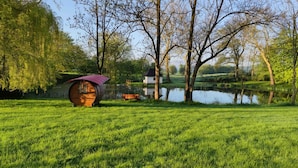 A serene park with a wooden barrel house, a small white building, and a bench by a pond.