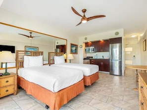 Une chambre d’hôtel avec deux lits, un coin cuisine, un ventilateur de plafond et un grand miroir.