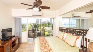 Une chambre d’hôtel équipée d’un lit, d’une télévision, d’un balcon avec vue sur la ville et d’un ventilateur de plafond.