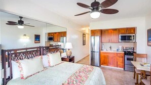 Une chambre à coucher comprenant un lit, un ventilateur de plafond, une table de chevet et une commode.
