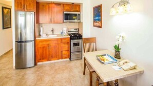 Une cuisine compacte dotée de meubles en bois, d’un réfrigérateur en acier inoxydable, d’un four à micro-ondes, d’un four traditionnel et d’une table à manger avec une chaise.