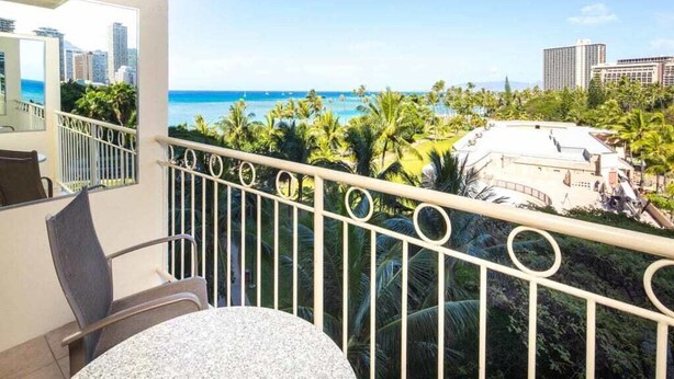 A balcony with a view of the ocean and palm trees.