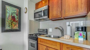A kitchen with wooden cabinets, a stainless steel stove, a microwave, and a sink. - Modern Ocean View W/Lanai and A/C - Waikīkī Shore #704 (HONOLULU)
