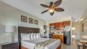 A hotel room with a bed, a desk, a chair, a ceiling fan, and a kitchenette. - Modern Ocean View W/Lanai and A/C - Waikīkī Shore #704 (HONOLULU)