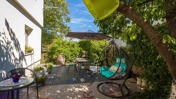 A patio with a hanging chair, a table, and a hanging umbrella.