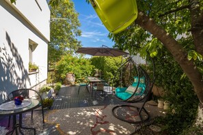 A patio with a hanging chair, a table, and a hanging umbrella. - Cozy Home With Private Garden (Jelenje)