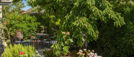 Un jardin avec un chemin en pierre, des plantes en pot et une table entourée de chaises.
