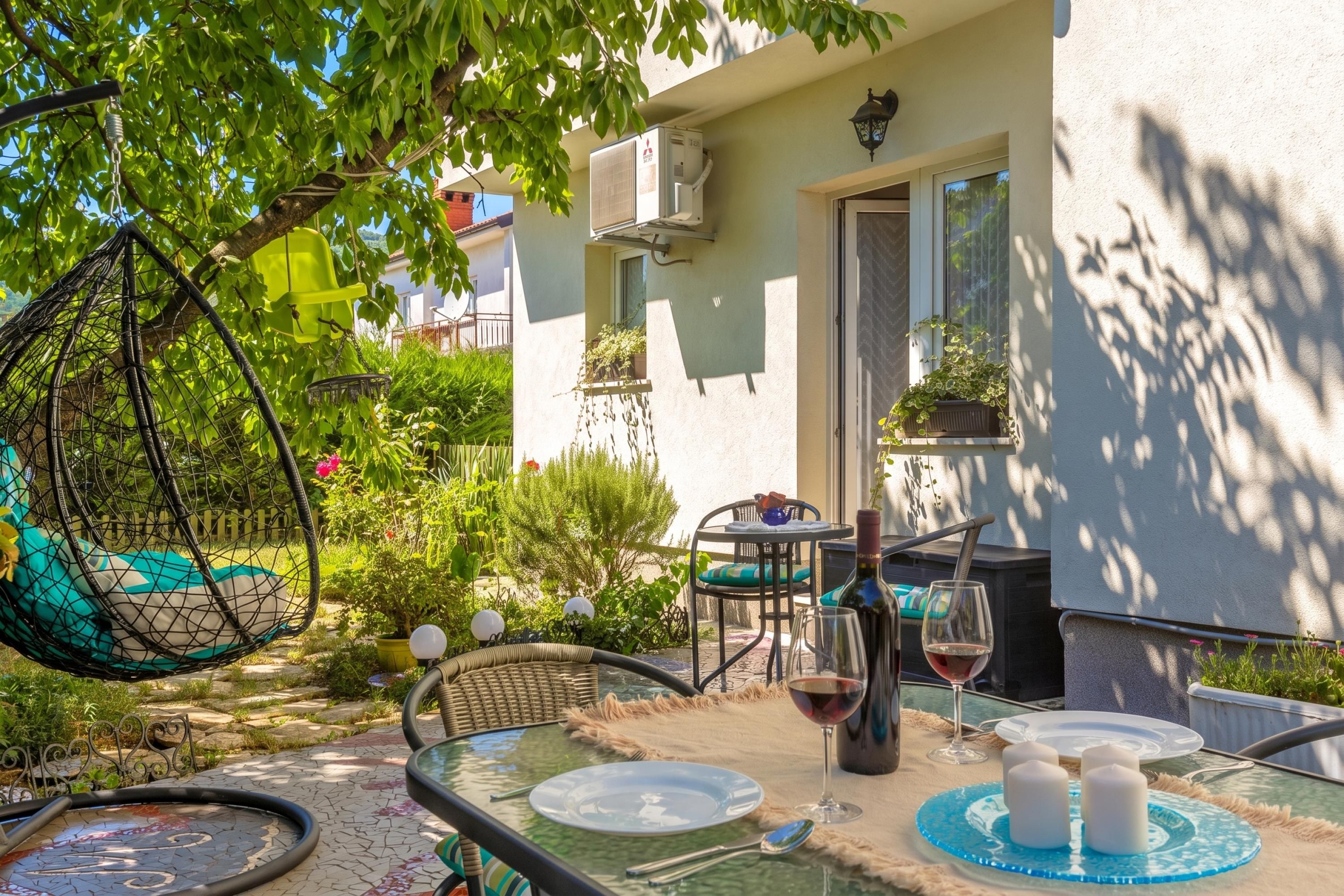 An outdoor seating area with a hanging chair, a table set for two, and a potted plant.