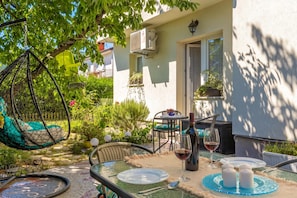 An outdoor seating area with a hanging chair, a table set for two, and a potted plant. - Cozy Home With Private Garden (Jelenje)