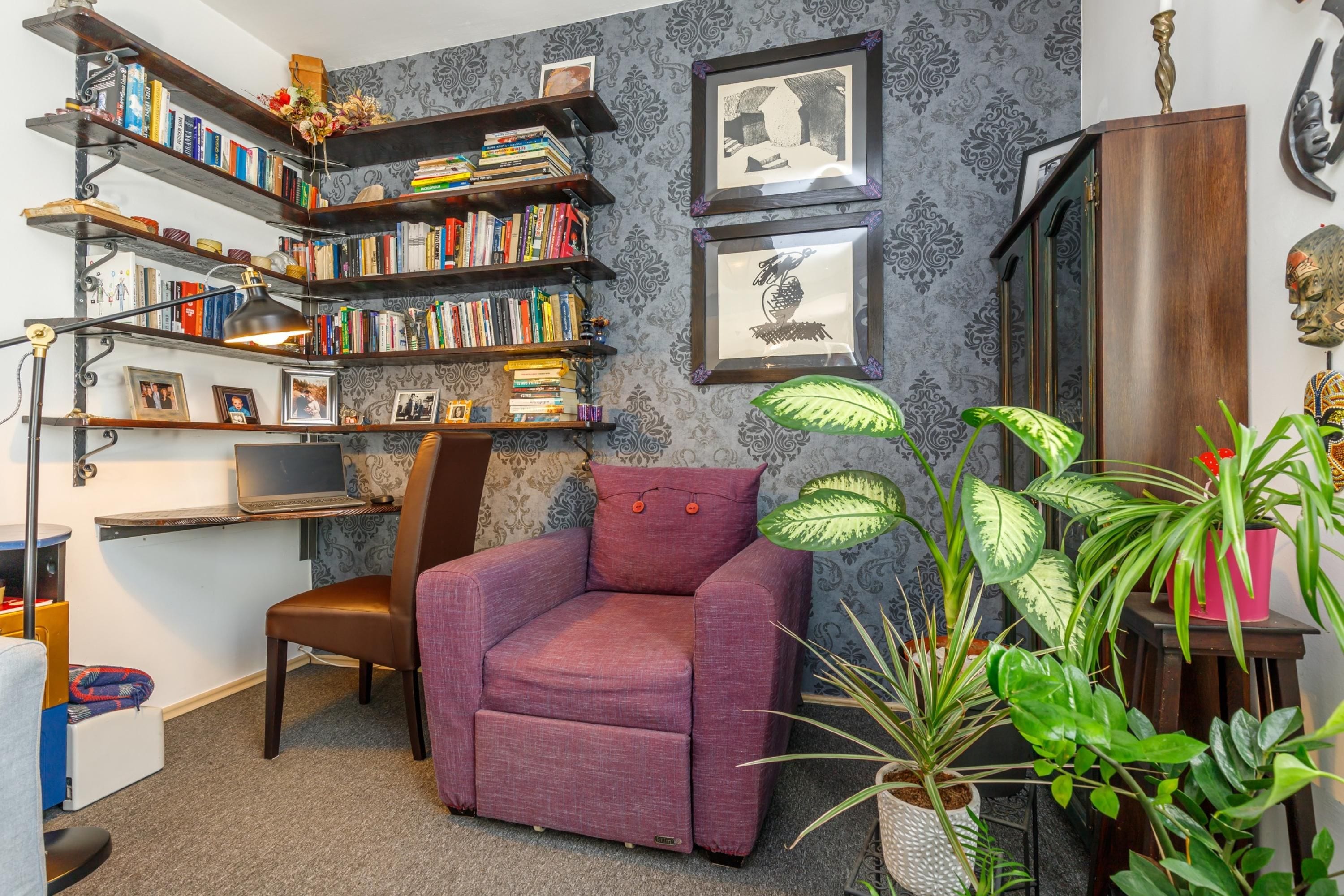 A cozy reading nook with a purple armchair, bookshelves, and framed artwork.