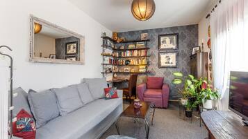 Una sala de estar con un sofá gris, una mesa de centro, una estantería, un sillón y un televisor.