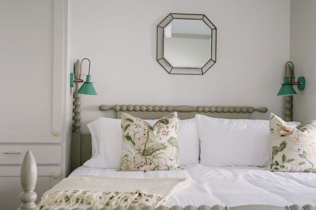 A bedroom with a bed, two wall-mounted lamps, a mirror, and a dresser.