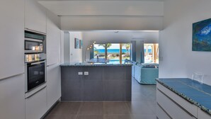 Uma cozinha moderna com ilha central, forno embutido e vista para o oceano.