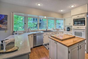 A modern kitchen with white cabinetry, a built-in dishwasher, a microwave, and a large window providing a view of greenery outside.