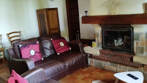 A living room with a leather sofa, a white table, a fireplace, and a clock on the wall. - Charming Cottage Near Bercé Forest: Fireplace, Billiards, Garden, Close to Hiking & Cycling Trails (Thoiré-sur-Dinan)