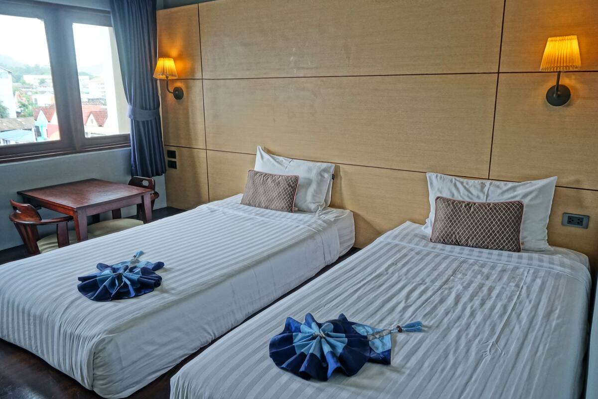 Two beds with white linens, a wooden nightstand, a small table, and two wall-mounted lamps.
