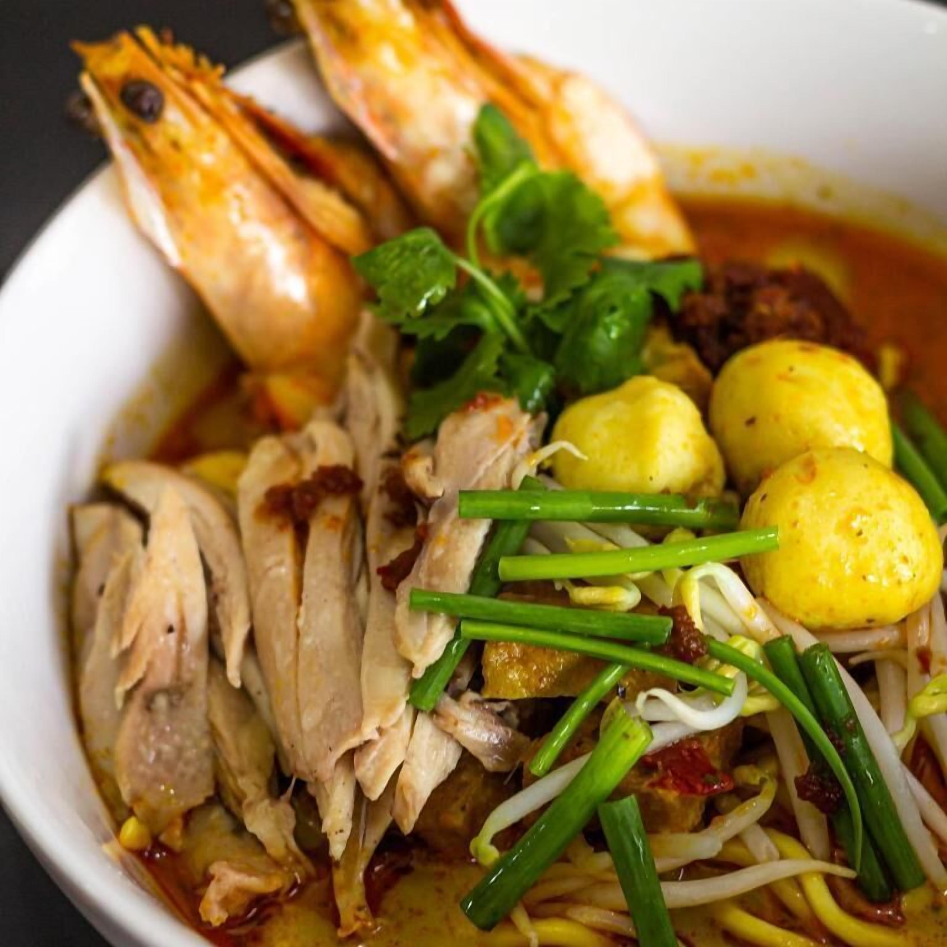 Eine Schüssel Nudelsuppe mit Hühnchen, Garnelen und gekochten Eiern, garniert mit frischen Zutaten.