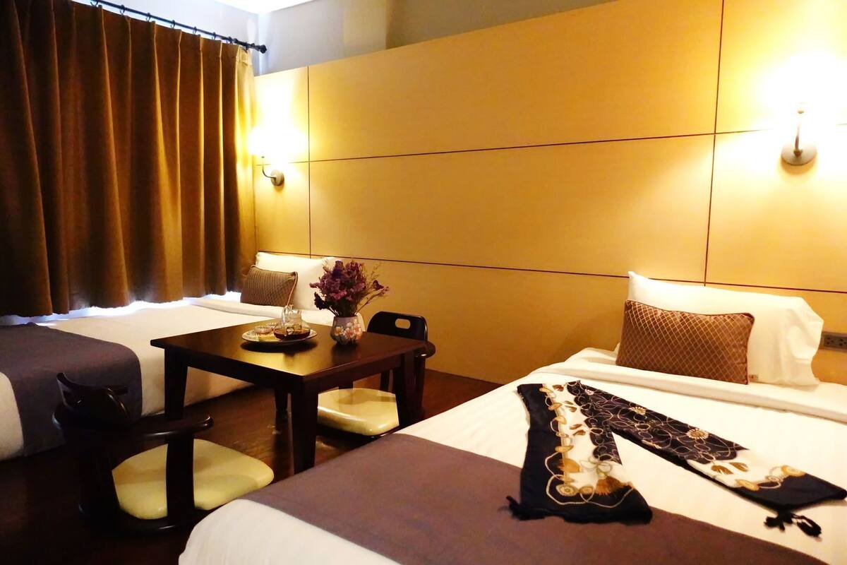 A hotel room with two beds, a small table with a vase, and a lamp.