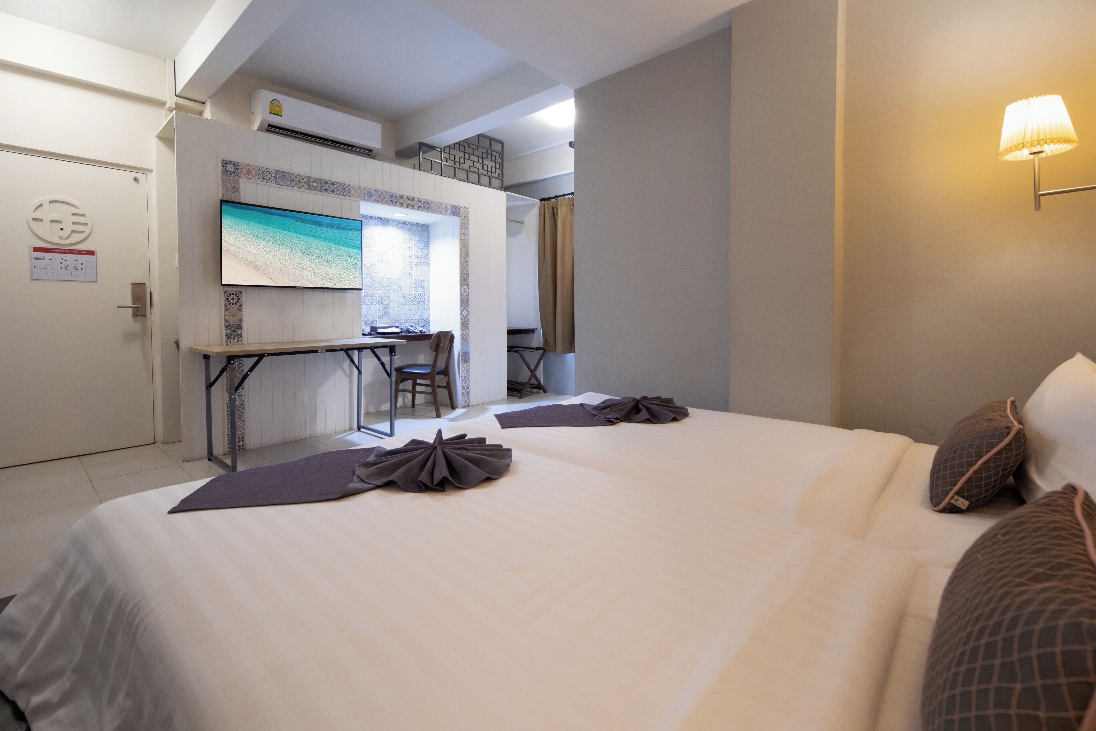 A hotel room with two beds, a desk with a chair, a TV on the wall, and a bathroom with a shower curtain.