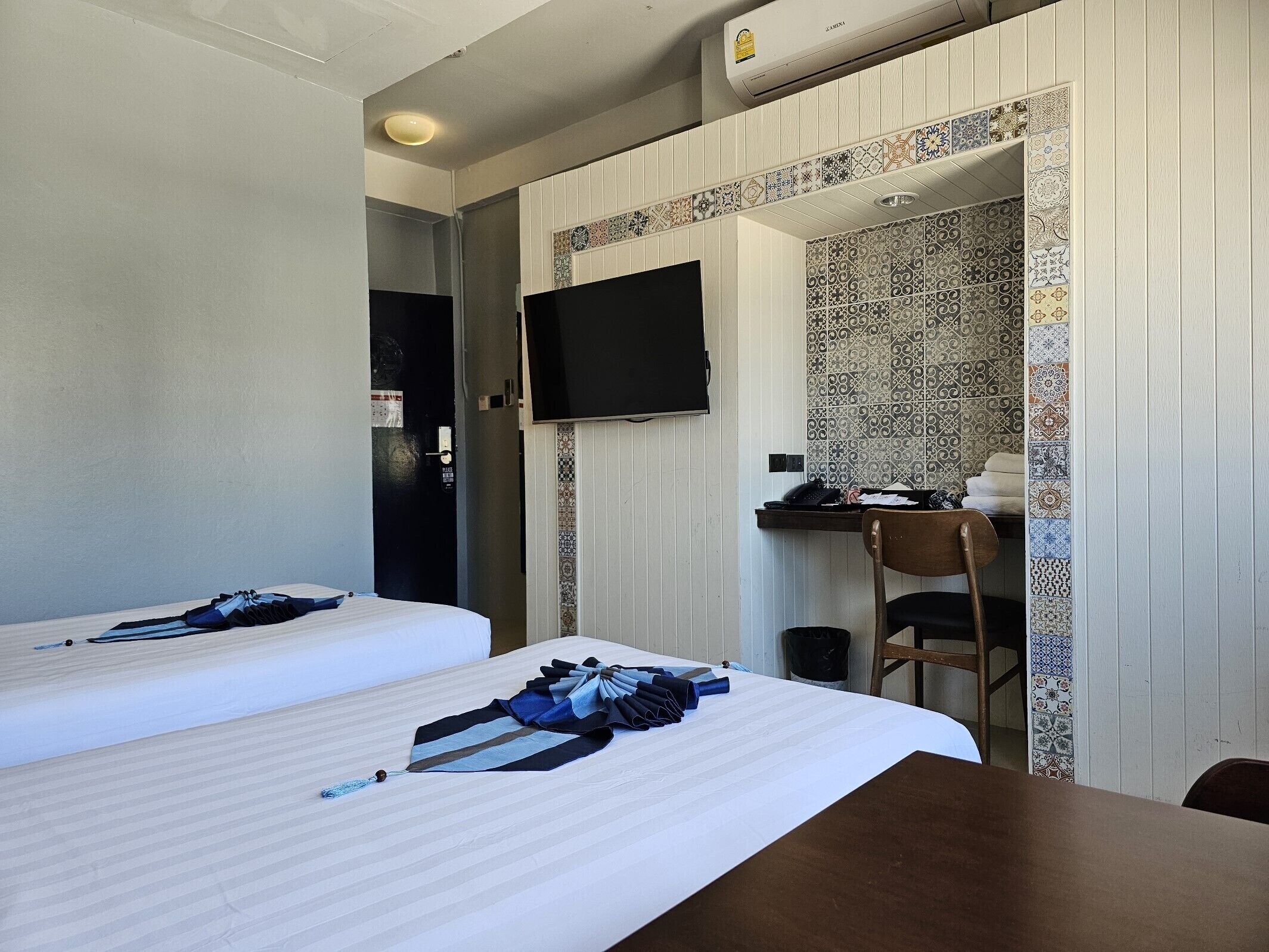 A hotel room with two beds, a desk with a chair, a television, and a bathroom door.