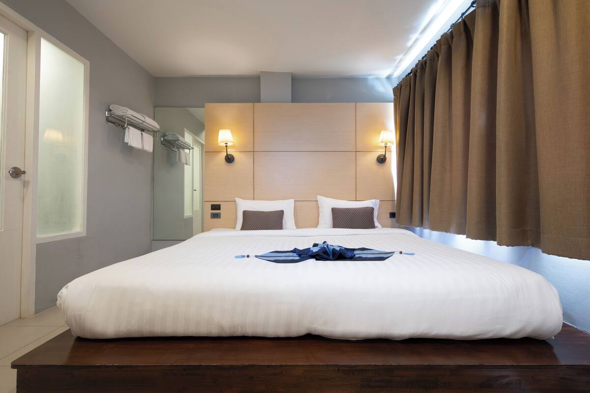 A hotel room with a large bed, a wooden headboard, two wall-mounted lamps, and a window with curtains.