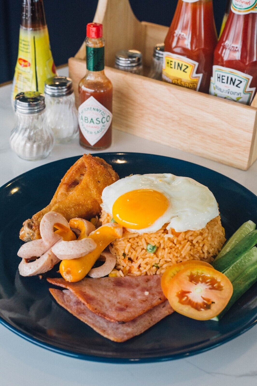 A plate of breakfast food including fried egg, sausage, bacon, and rice.
