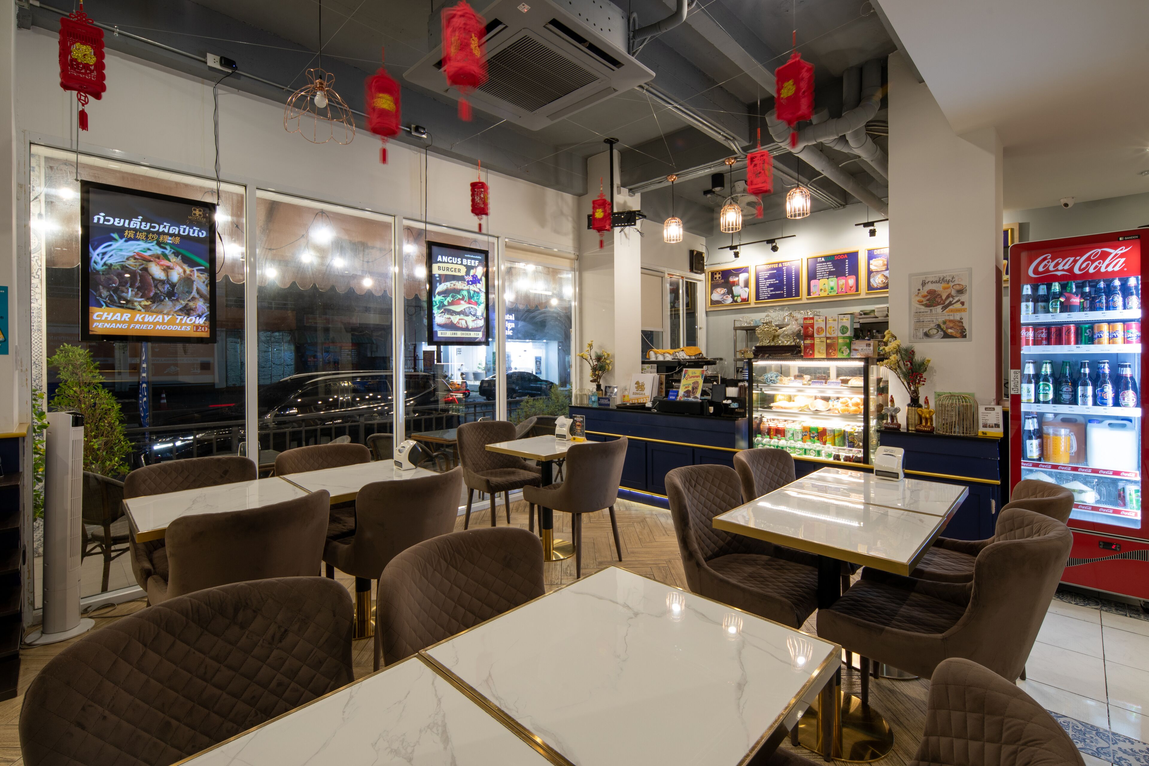 A restaurant interior with tables and chairs, a Coca-Cola refrigerator, and menu boards on the walls.