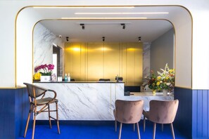 A modern reception area with marble countertops, a gold-toned reception desk, and two cushioned chairs. - Montree Phuket Hotel (Phuket)
