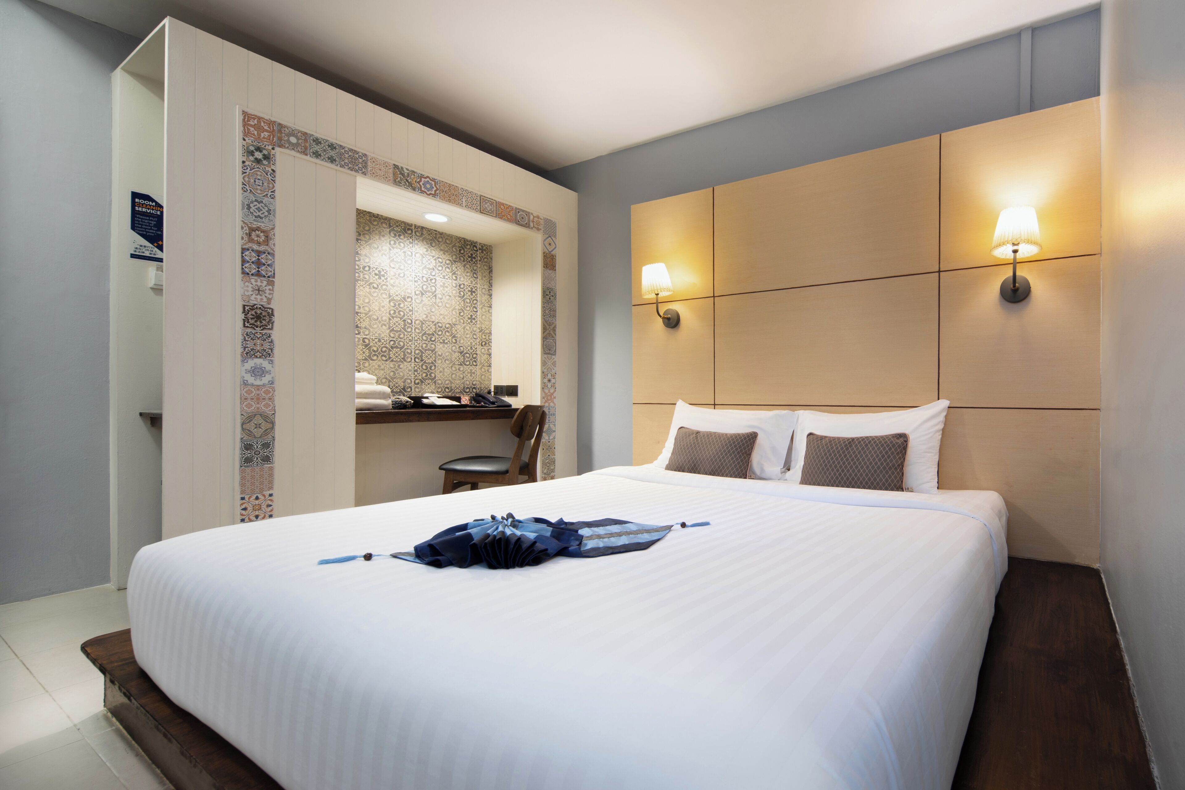 Habitación de hotel con una cama grande, un escritorio con silla, un baño pequeño y una lámpara de pared.