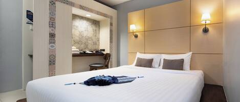 Habitación de hotel con una cama grande, un escritorio con silla, un baño pequeño y una lámpara de pared.