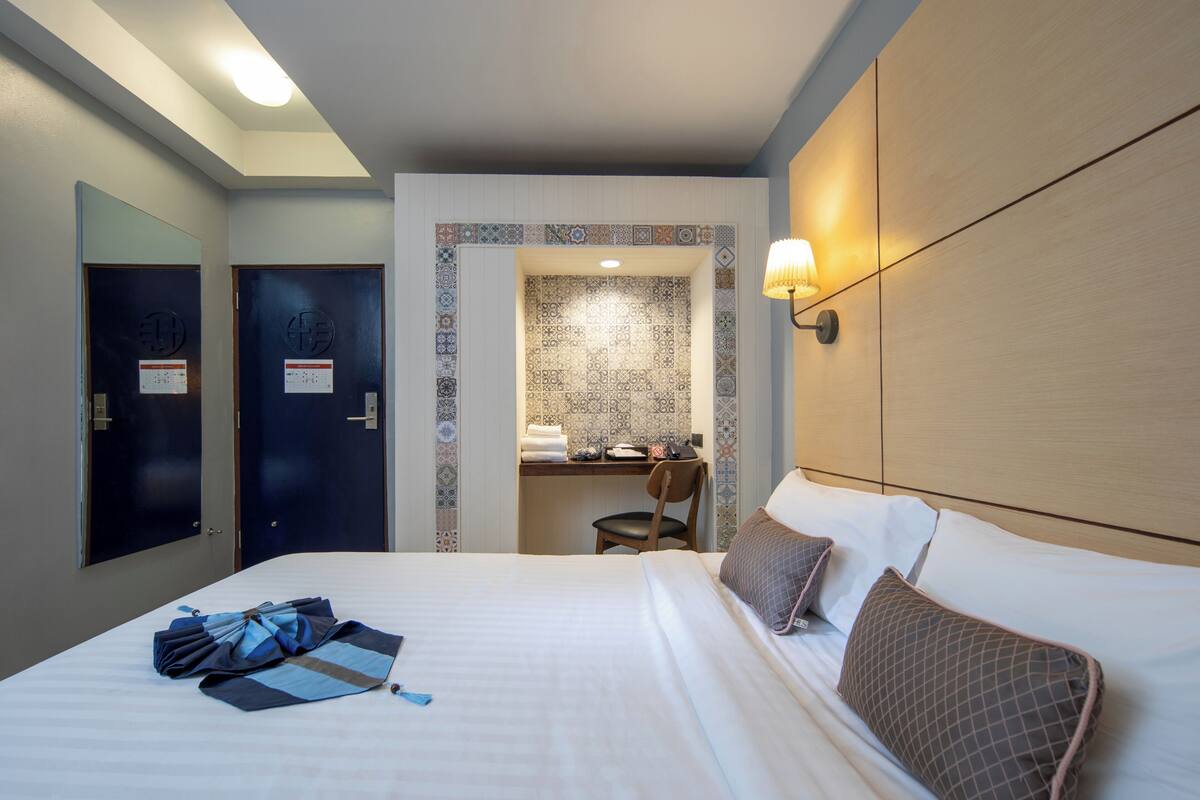 A hotel room with a neatly made bed, a desk with a chair, and a bathroom visible through an open door.