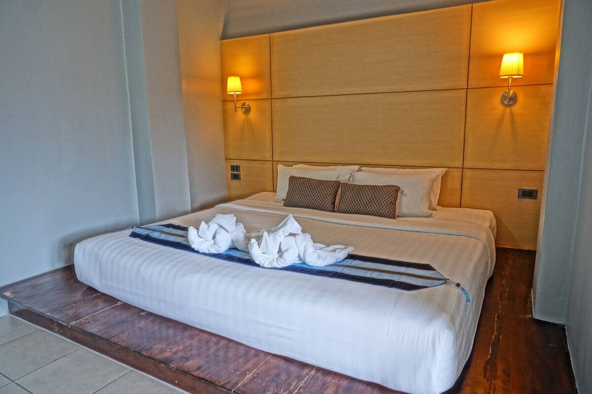 A hotel room with a large bed, two wall-mounted lamps, and a wooden headboard.
