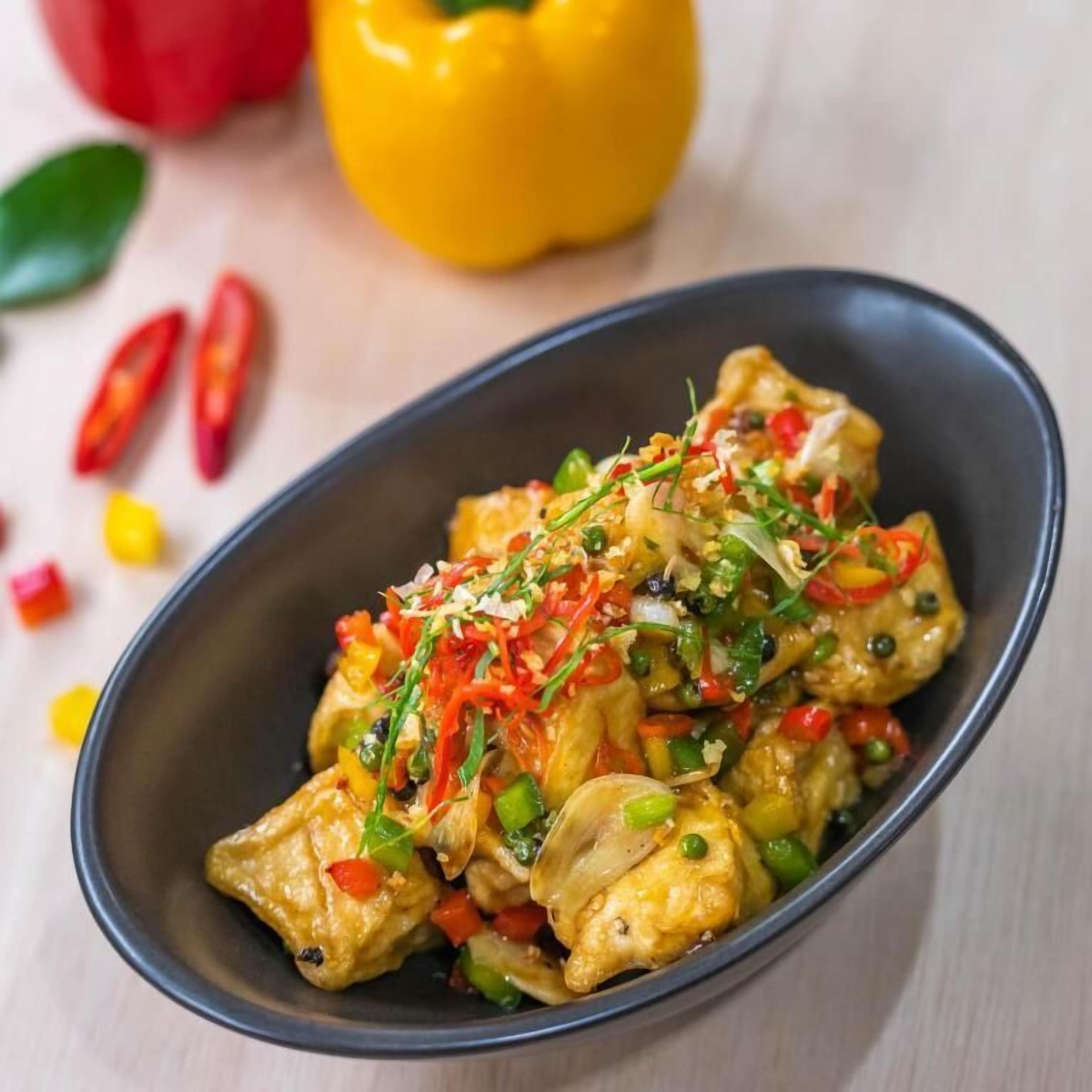 Un piatto di pollo saltato in padella con verdure, guarnito con cipollotti e fettine di peperoncino rosso.