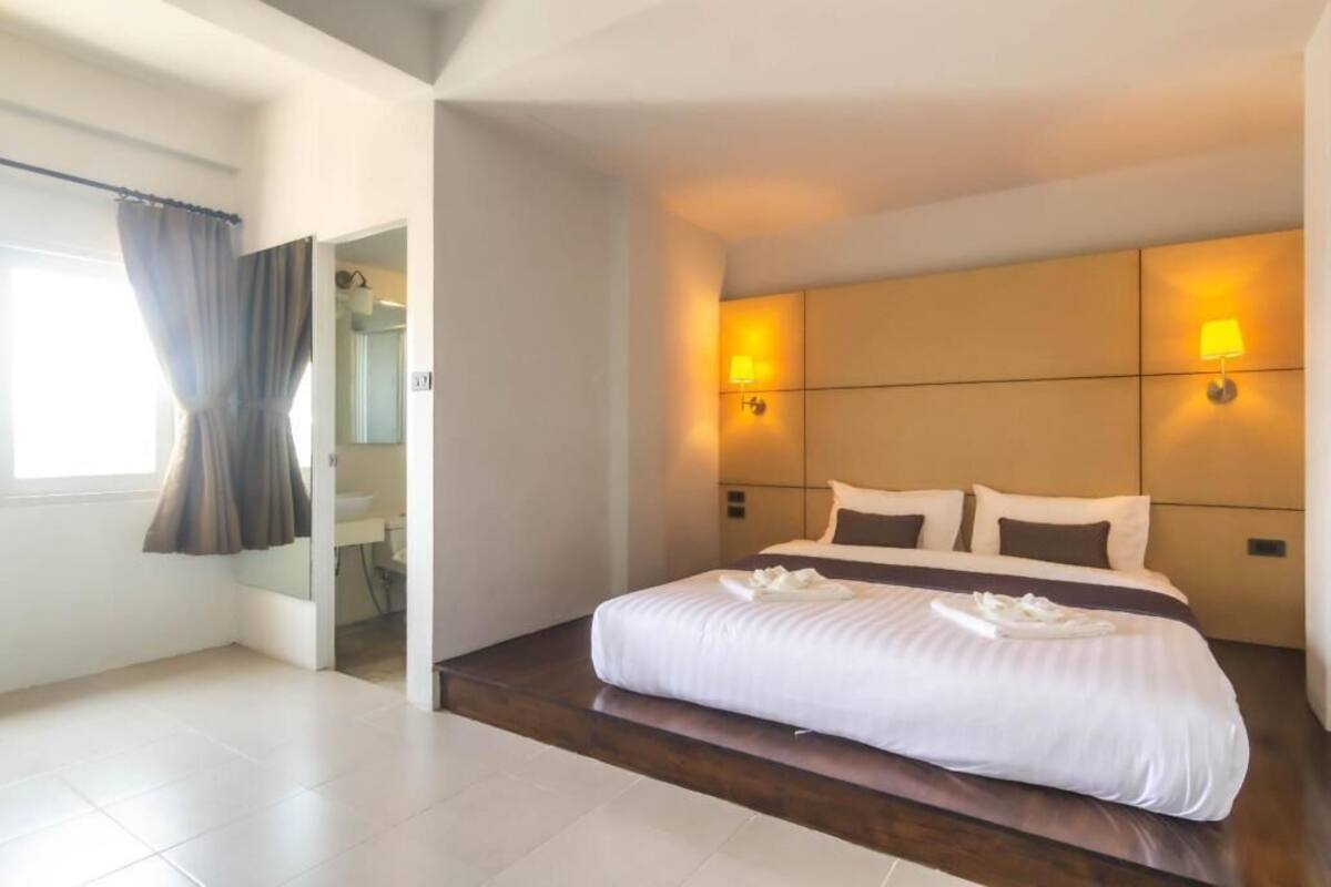 A hotel room with a large bed, two wall-mounted lights, a bathroom with a mirror, and a window with curtains.