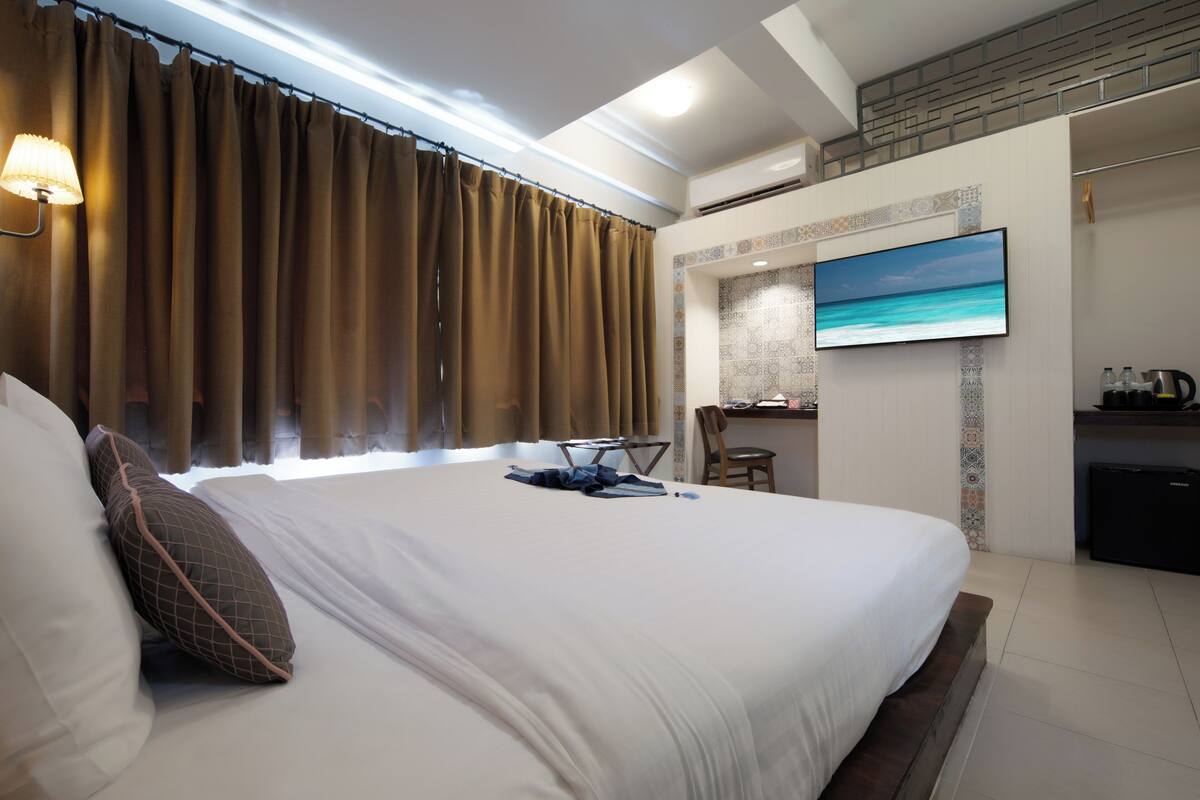 A hotel room with a large bed, a TV mounted on the wall, and a desk with a chair.