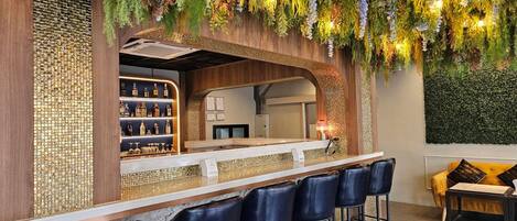 A bar area with a wooden counter, black leather bar stools, and a wall decorated with hanging plants.